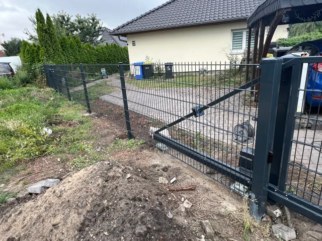 Tor mit Gitterfüllung neben einem Stabmattenzaun