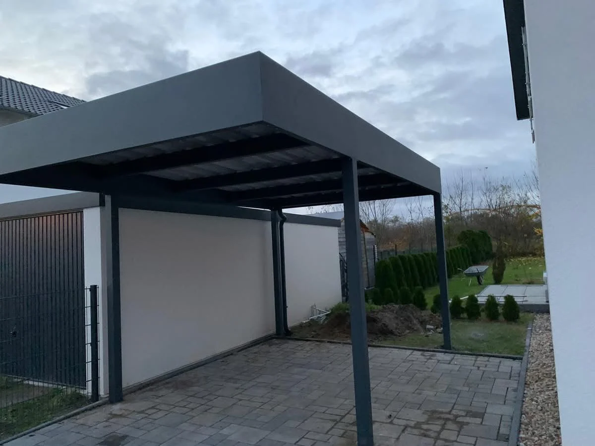Dunkle Carportkonstruktion neben einer hellen Garagenwand
