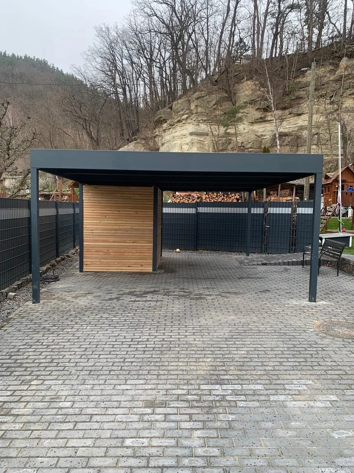 Anthrazitfarbener Carport mit teilweiser Verkleidung in Holzoptik