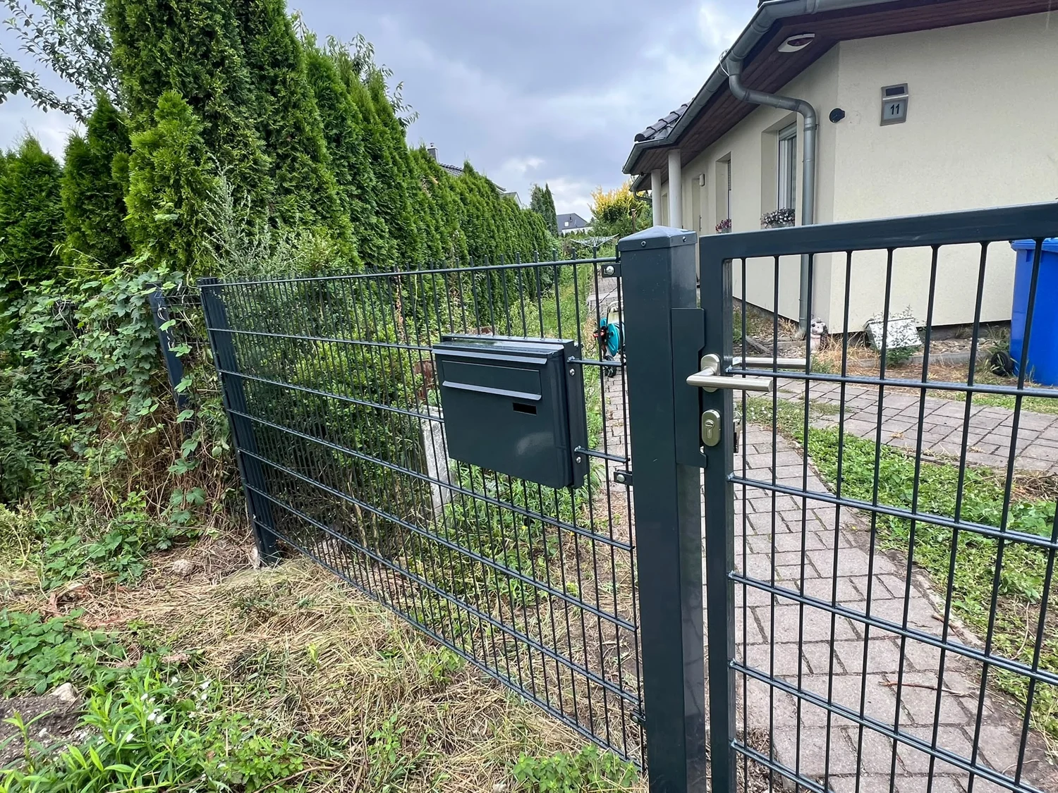 Detail einer Stabmatten-Gartentür: Griff und Schließzylinder am Pfosten neben einem Briefkasten