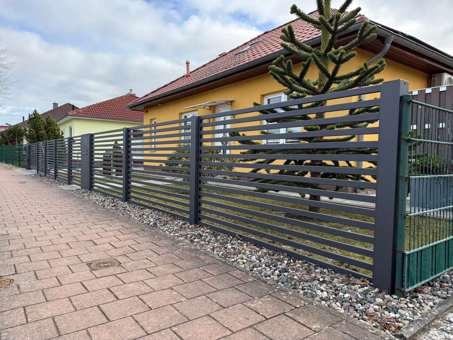 Anthrazitfarbene Zaunfelder mit waagerechter Füllung an einem gelben Haus