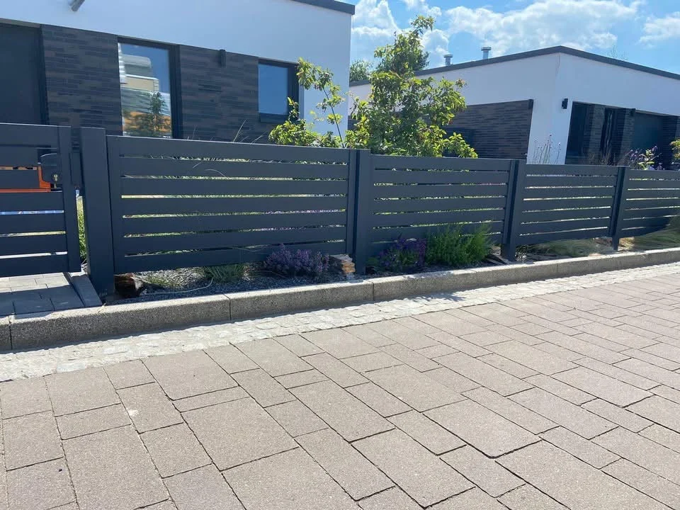 Anthrazitfarbener Zaun mit waagerechten Profilen vor einem hellen Haus